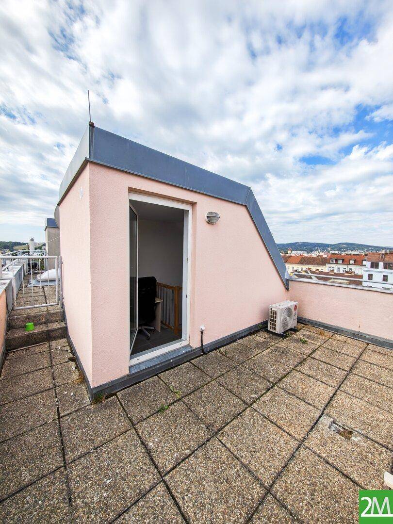 Dachterrasse mit Betonplatten und einem kleinen Gebäude, bietet einen weiten Blick über die Stadt.