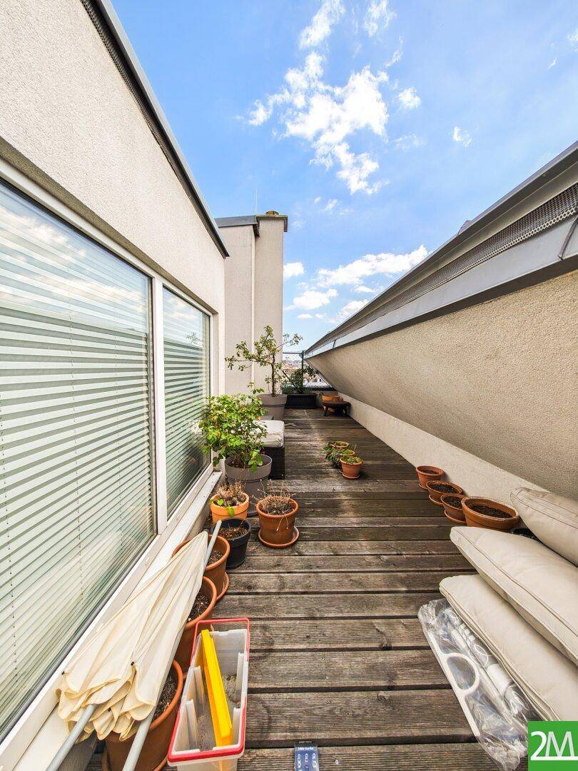 Weitere Ansicht der Dachterrasse mit Holzbelag, vielen Topfpflanzen und Sonnenschirm.