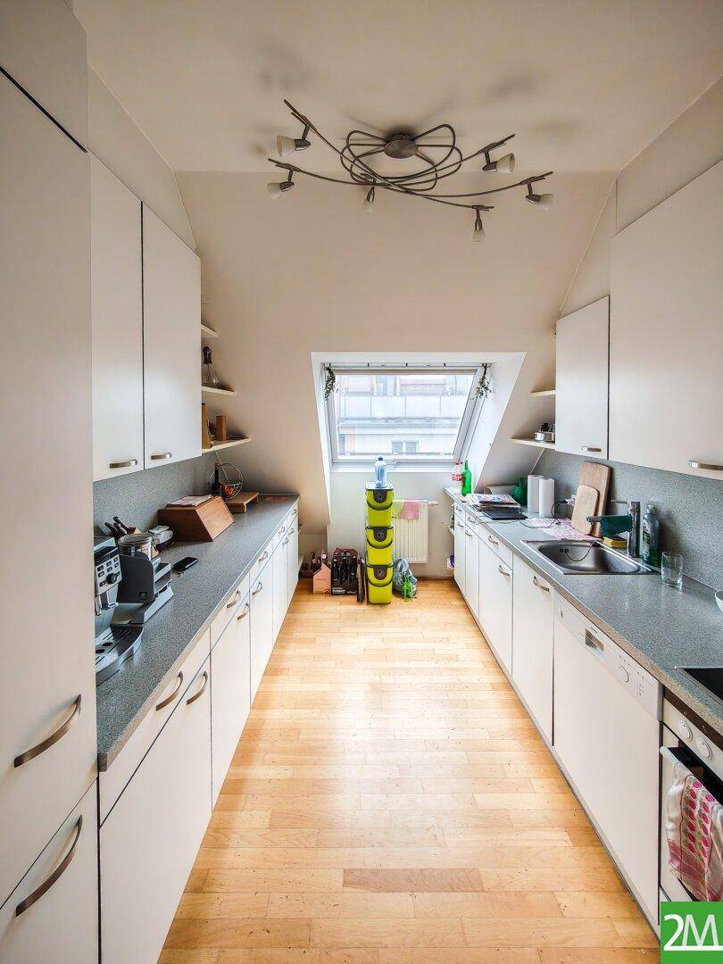Schmale Küche im Dachgeschoss mit weißen Schränken, grauen Arbeitsplatten und Dachfenster.