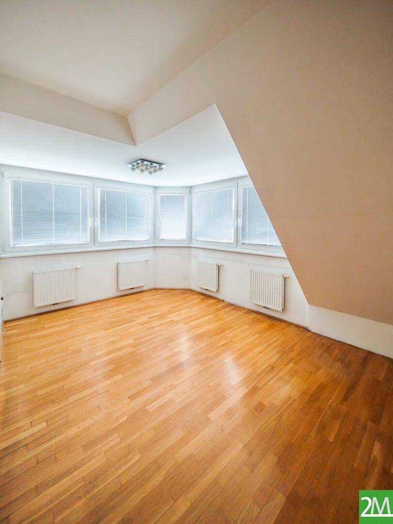 Leerer Raum im Dachgeschoss mit vielen Fenstern, Holzboden und schrägen Wänden.