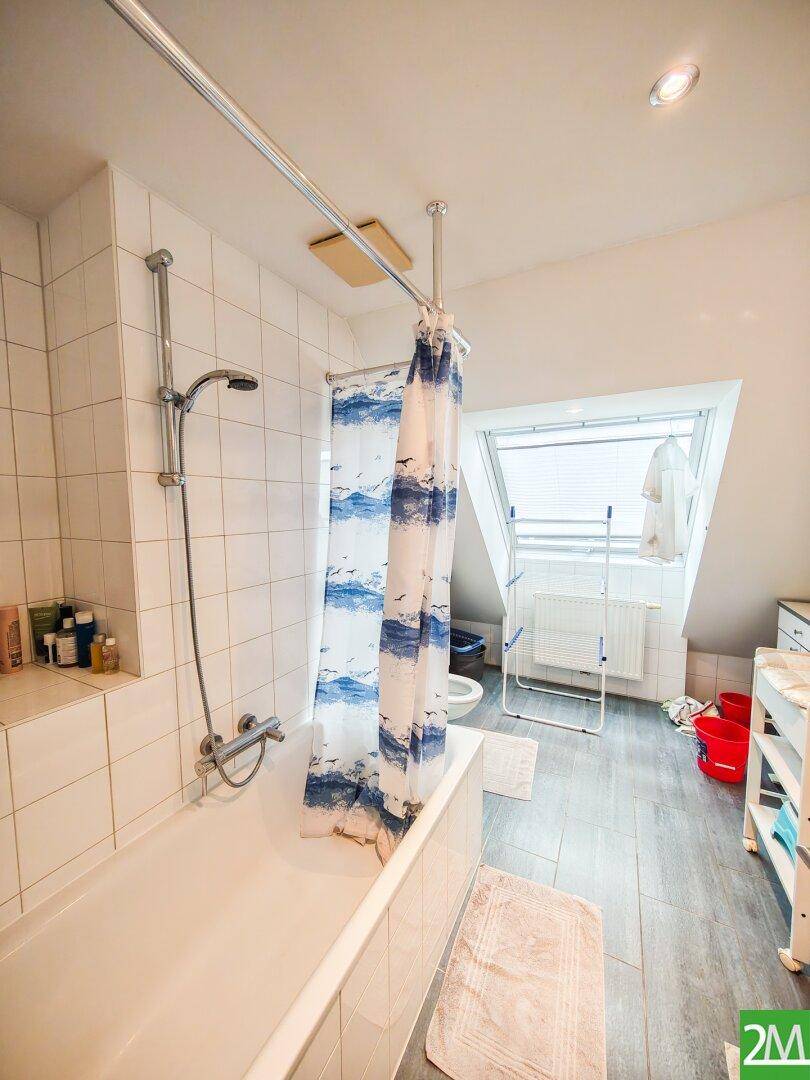 Badezimmer mit Badewanne, Duschvorhang, Dachfenster und hellen Fliesen.