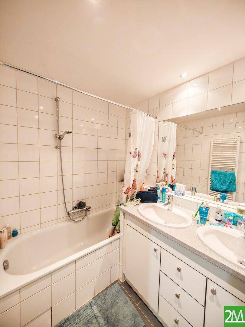 Badezimmer mit Doppelwaschbecken, großem Spiegel, Badewanne mit Duschfunktion und weißen Fliesen.