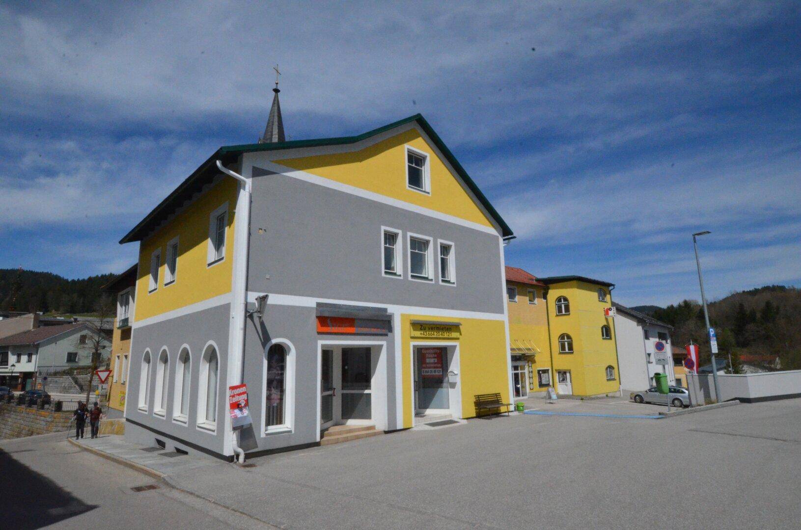 Außenansicht eines Gebäudes mit gelber und grauer Fassade und dekorativen Bogenfenstern.