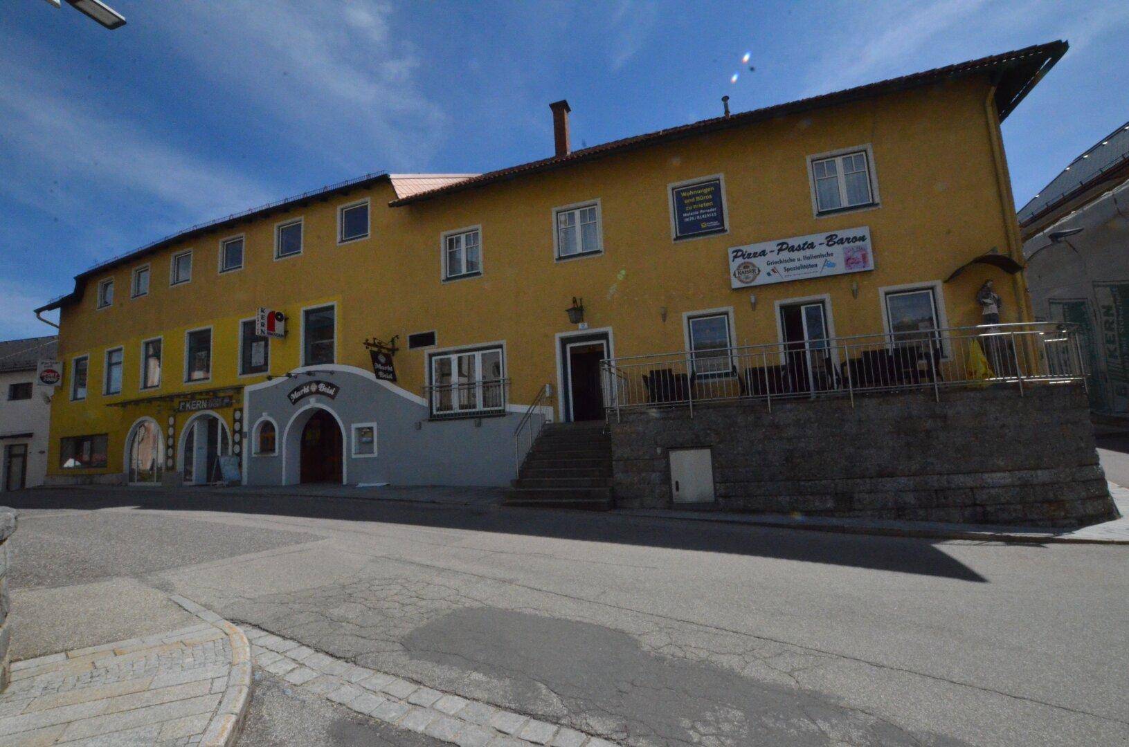 Langes gelbes Gebäude mit Restaurantbereich und Außenterrasse an einer Straße gelegen.