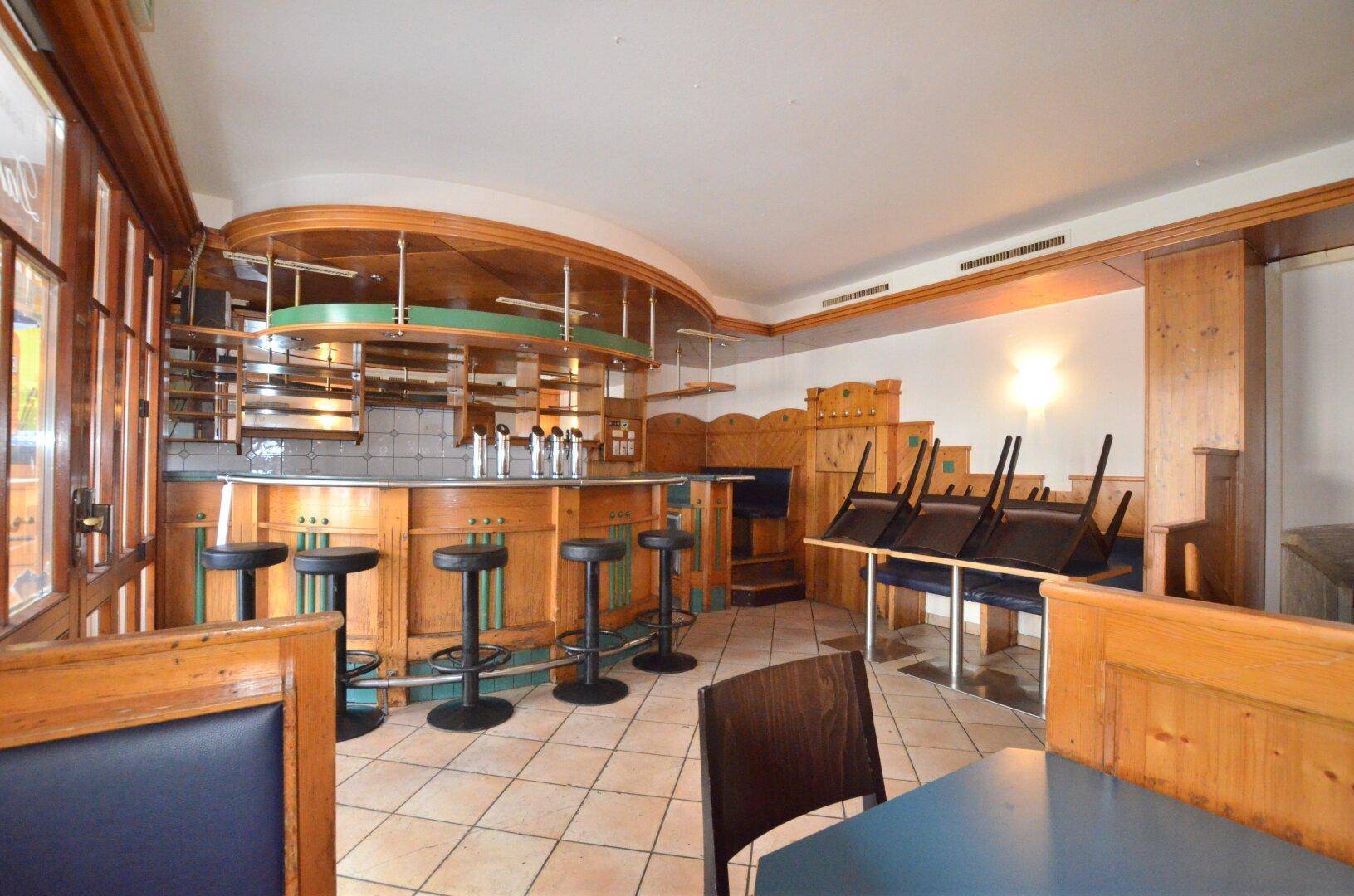 Traditionelle Bar mit Holzvertäfelung, Barhockern und gefliestem Boden.