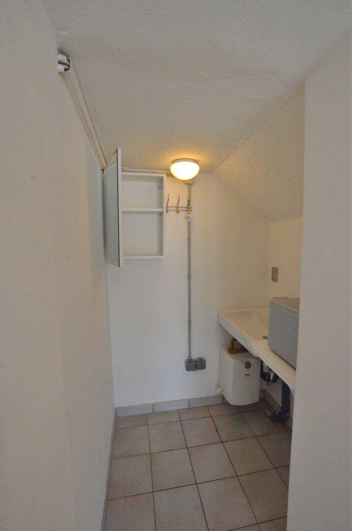 Kleiner Hauswirtschaftsraum mit Waschbecken, Fliesenboden und einfacher Beleuchtung.