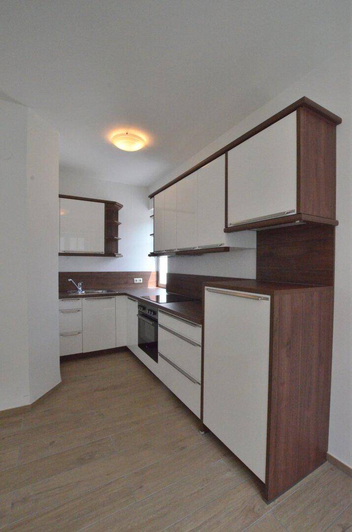 Moderne Einbauküche mit weißen und holzfarbenen Schränken und integriertem Backofen.