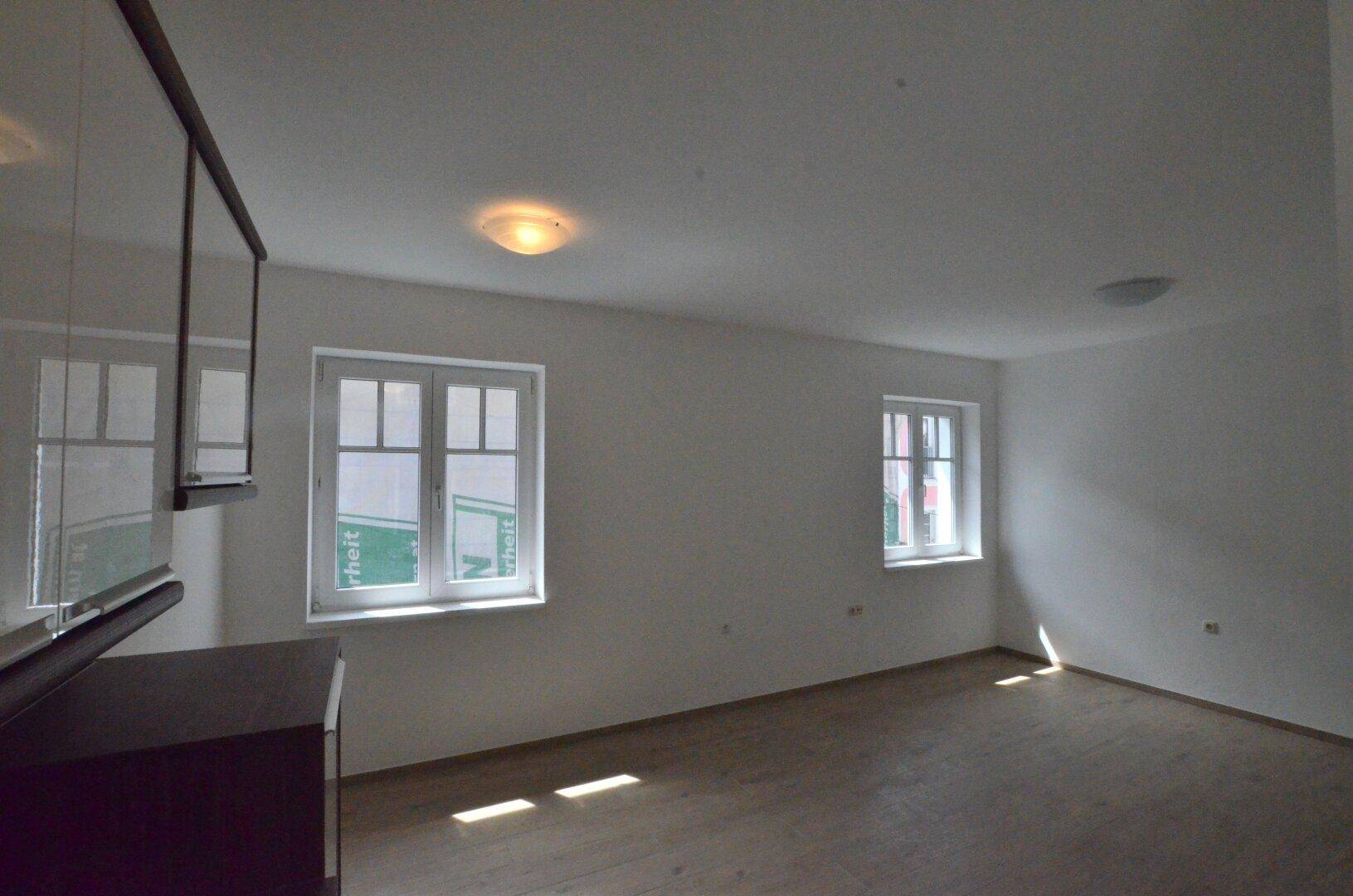Lichtdurchfluteter Wohnbereich mit Holzboden und zwei großen Fenstern.