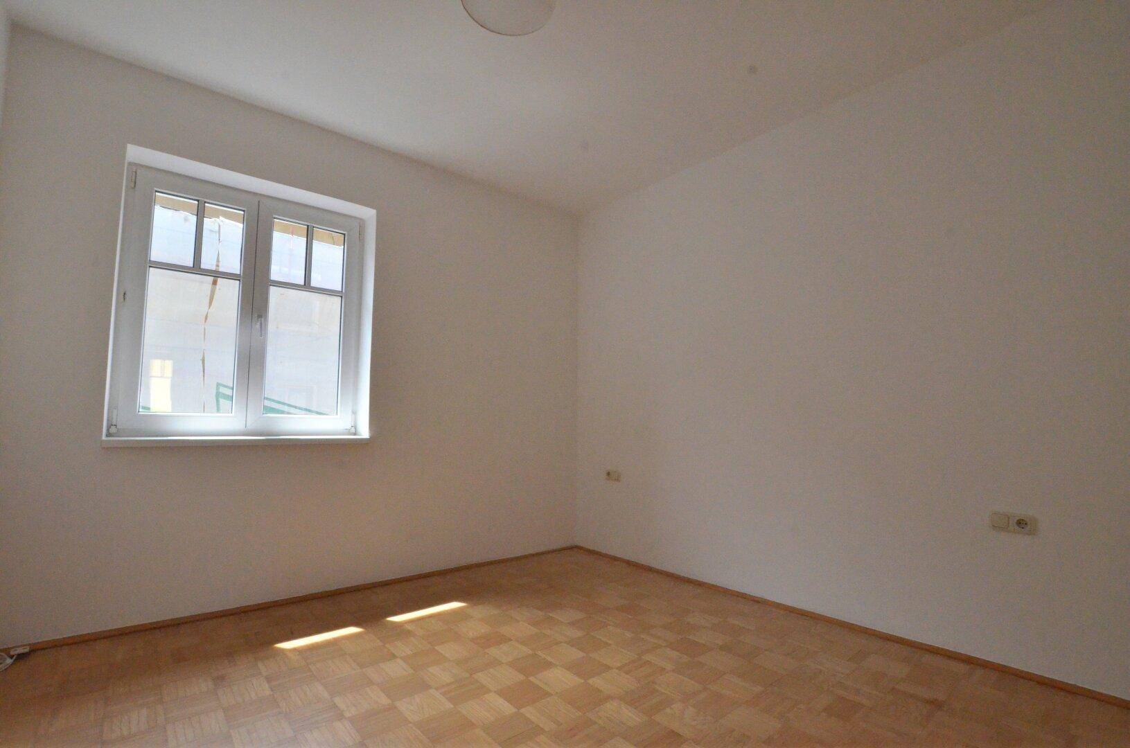 Helles Schlafzimmer mit Parkettboden und einem großen Fenster.