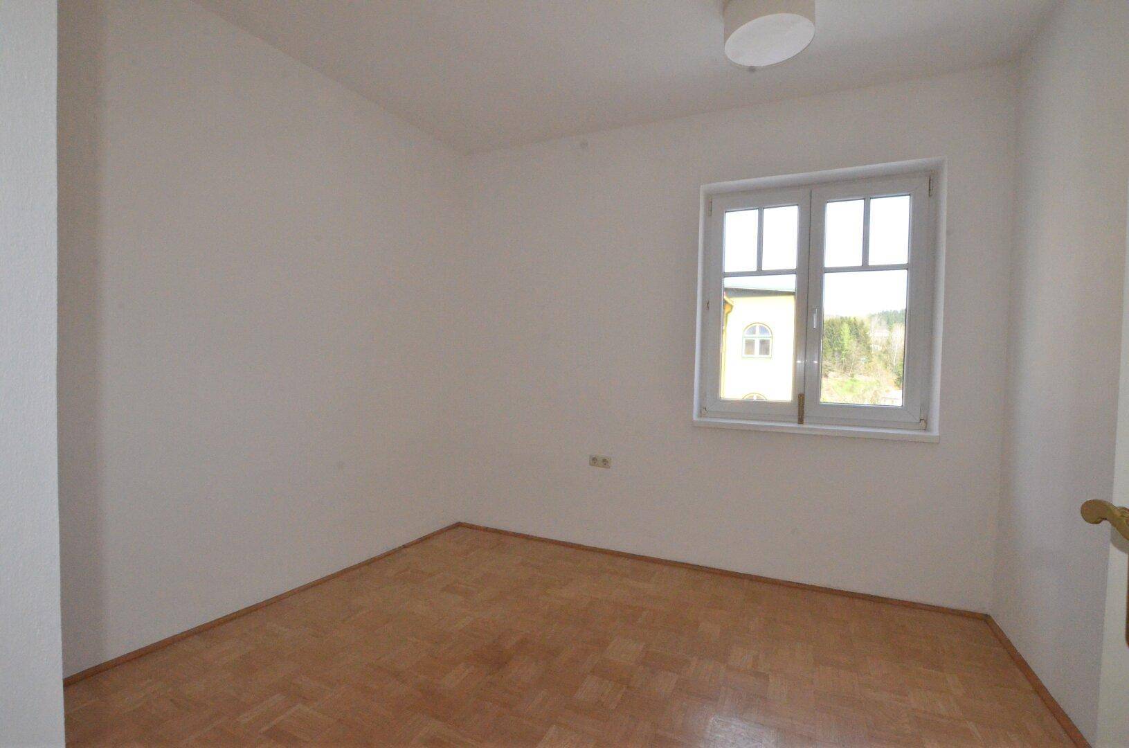 Geräumiges Schlafzimmer mit Parkettboden und einem Fenster mit Blick ins Grüne.