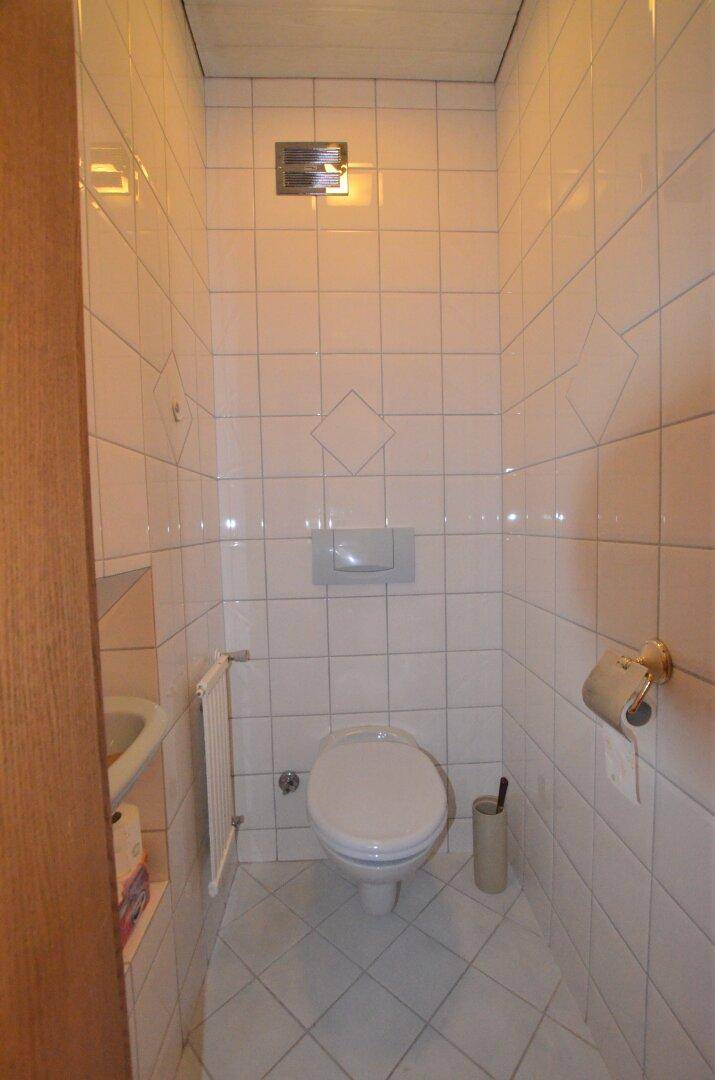 Kleines, vollständig gefliestes Gäste-WC mit wandhängender Toilette und kleinem Waschbecken.