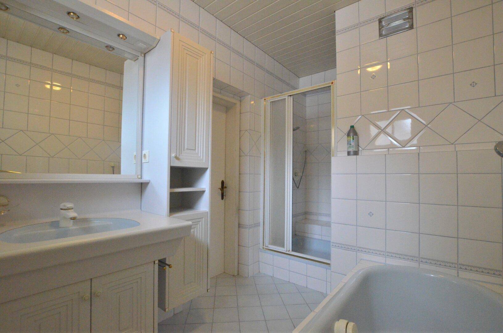 Helles Badezimmer mit Waschtisch, Spiegelschrank, Duschkabine und Badewanne, komplett gefliest.