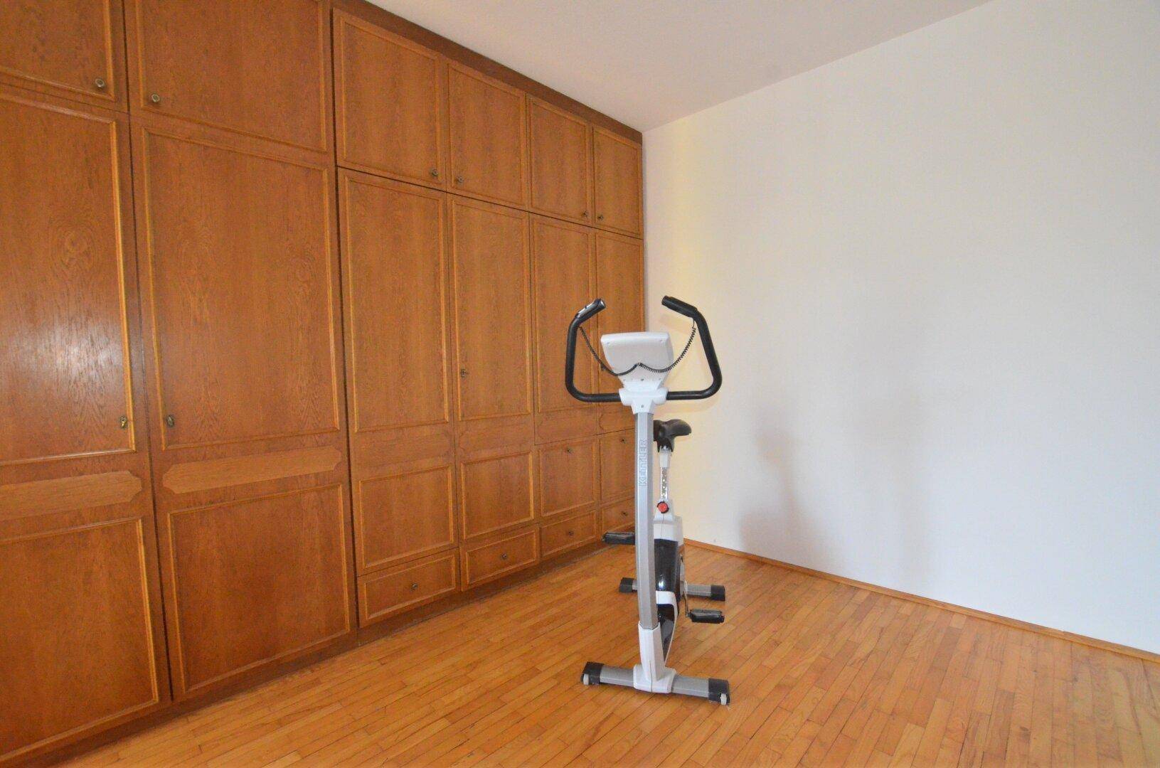 Zimmer mit Holzboden und großer Einbauschrankwand, ideal als Schlaf- oder Fitnessraum nutzbar.