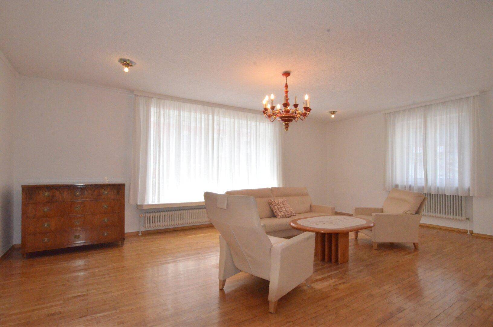 Geräumiges Wohnzimmer mit Holzboden, großen Fenstern und klassischer Möblierung, hell und einladend.