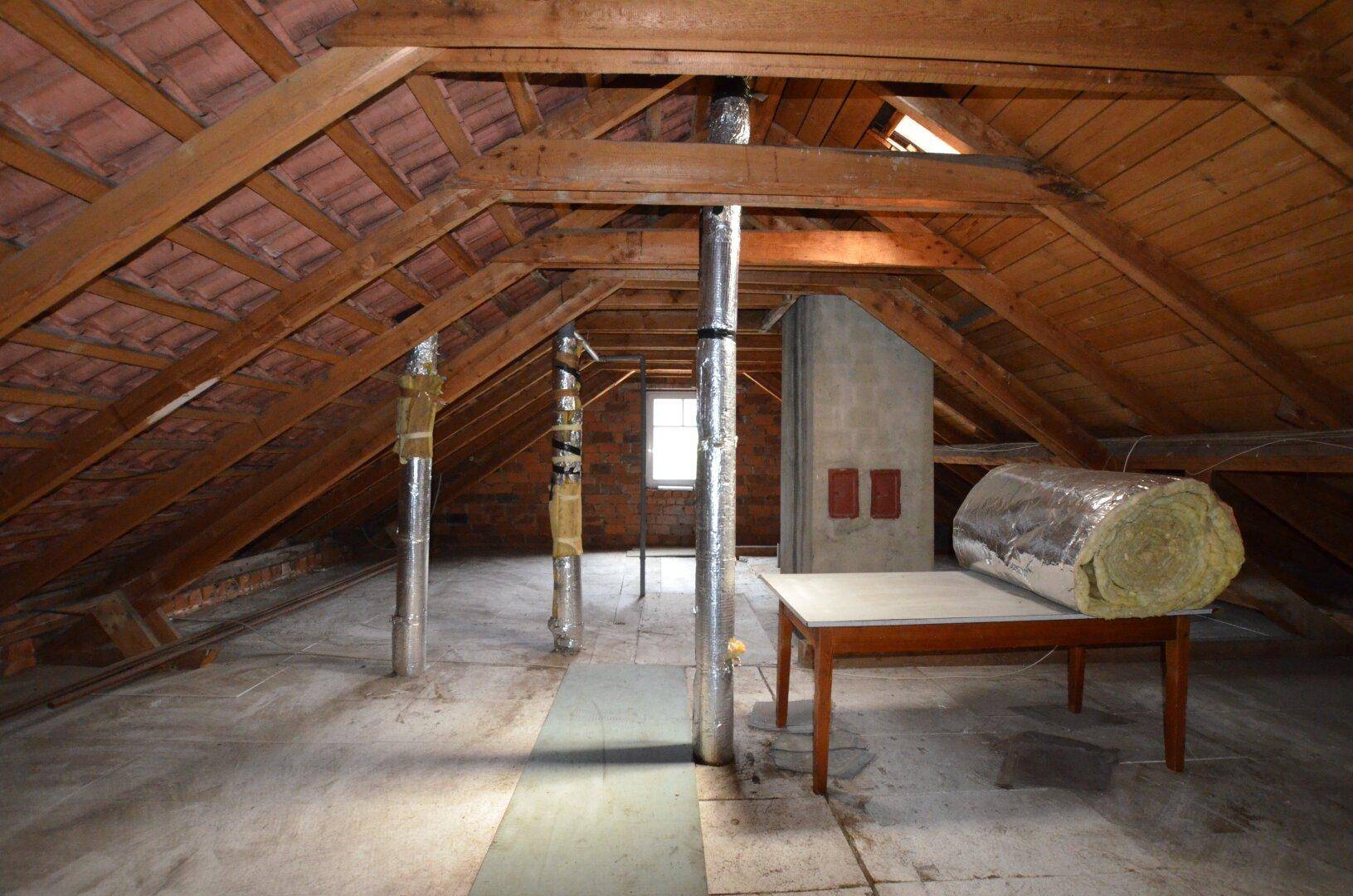 Unausgebauter Dachboden mit sichtbarer Holzkonstruktion und Isolationsmaterial, ideal für einen Umbau.