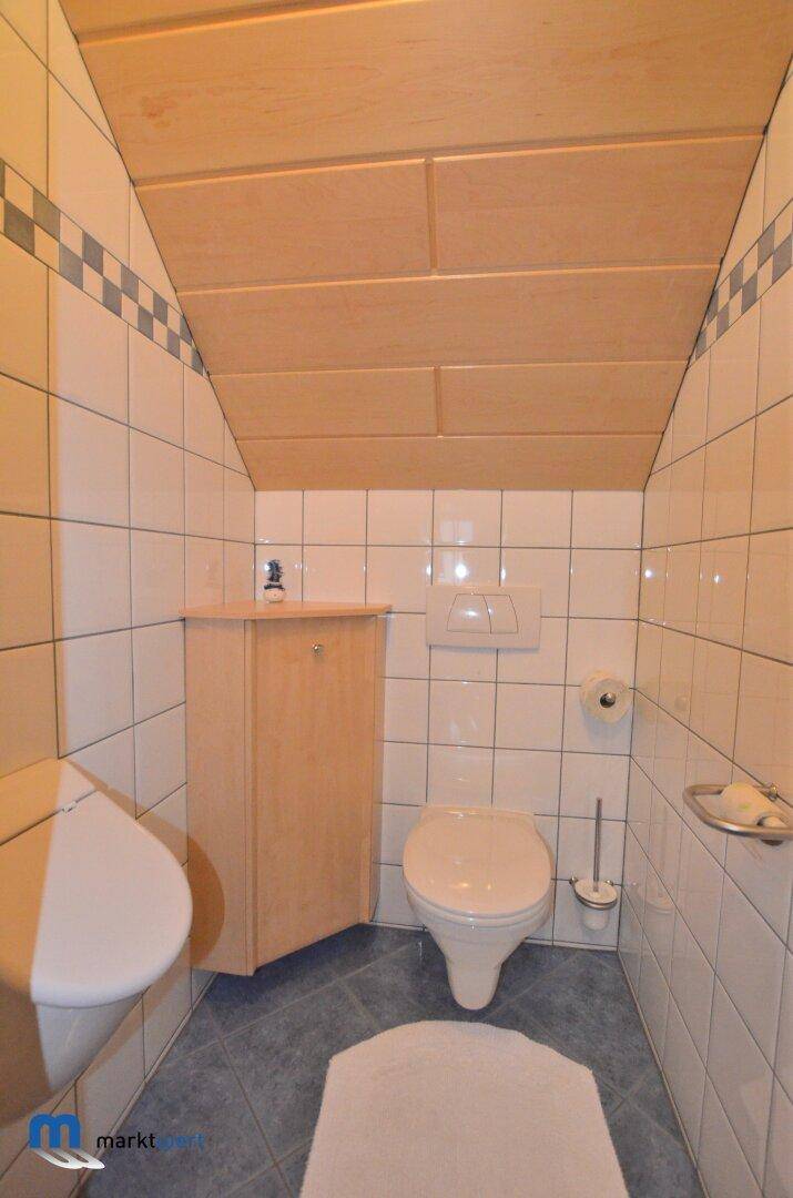 Kleines Gäste-WC mit Toilette, Waschbecken, Fliesen und Holzdeckenverkleidung.