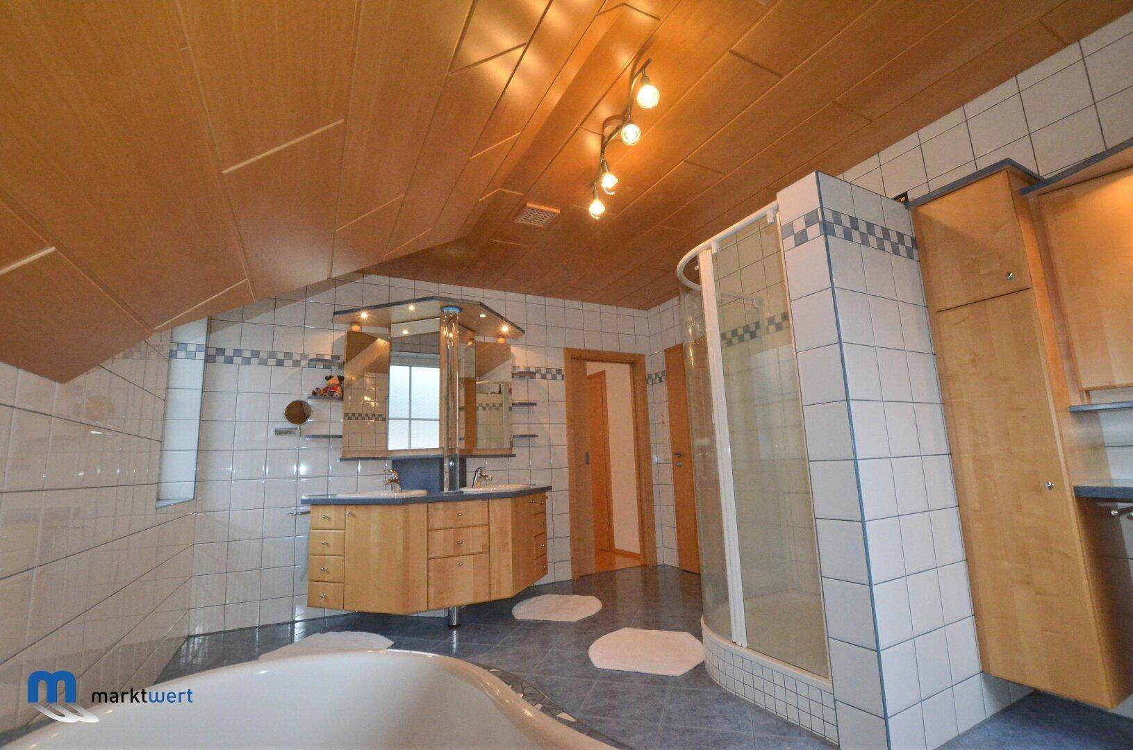 Helles Badezimmer mit Fenster, Badewanne, Duschkabine und Holzverkleidung an der Decke.