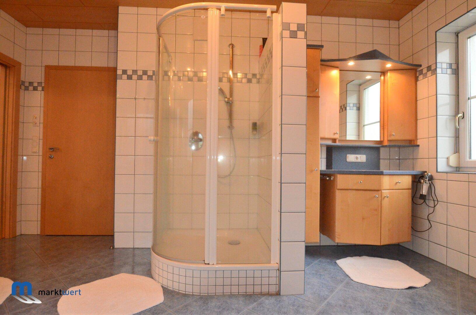Duschkabine und Waschtisch mit Spiegelschrank in einem gefliesten Badezimmer.