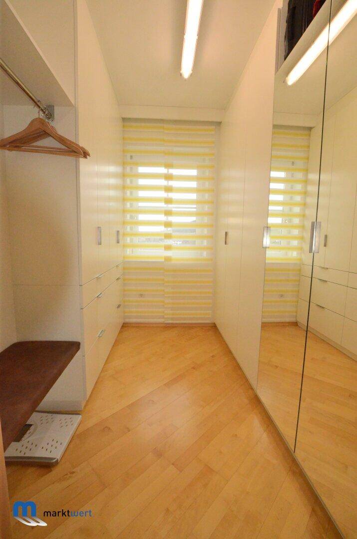 Geräumiger begehbarer Kleiderschrank mit Spiegelfronten und Fenster für Tageslicht.