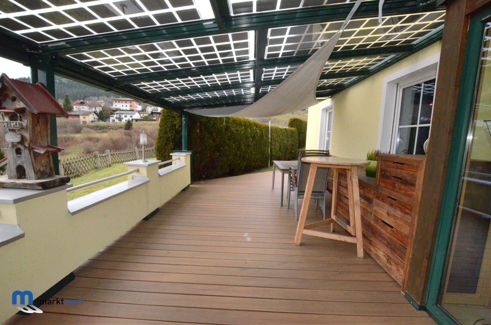 Überdachte Terrasse mit Holzdielenboden, Stehtisch und Blick auf die Landschaft.