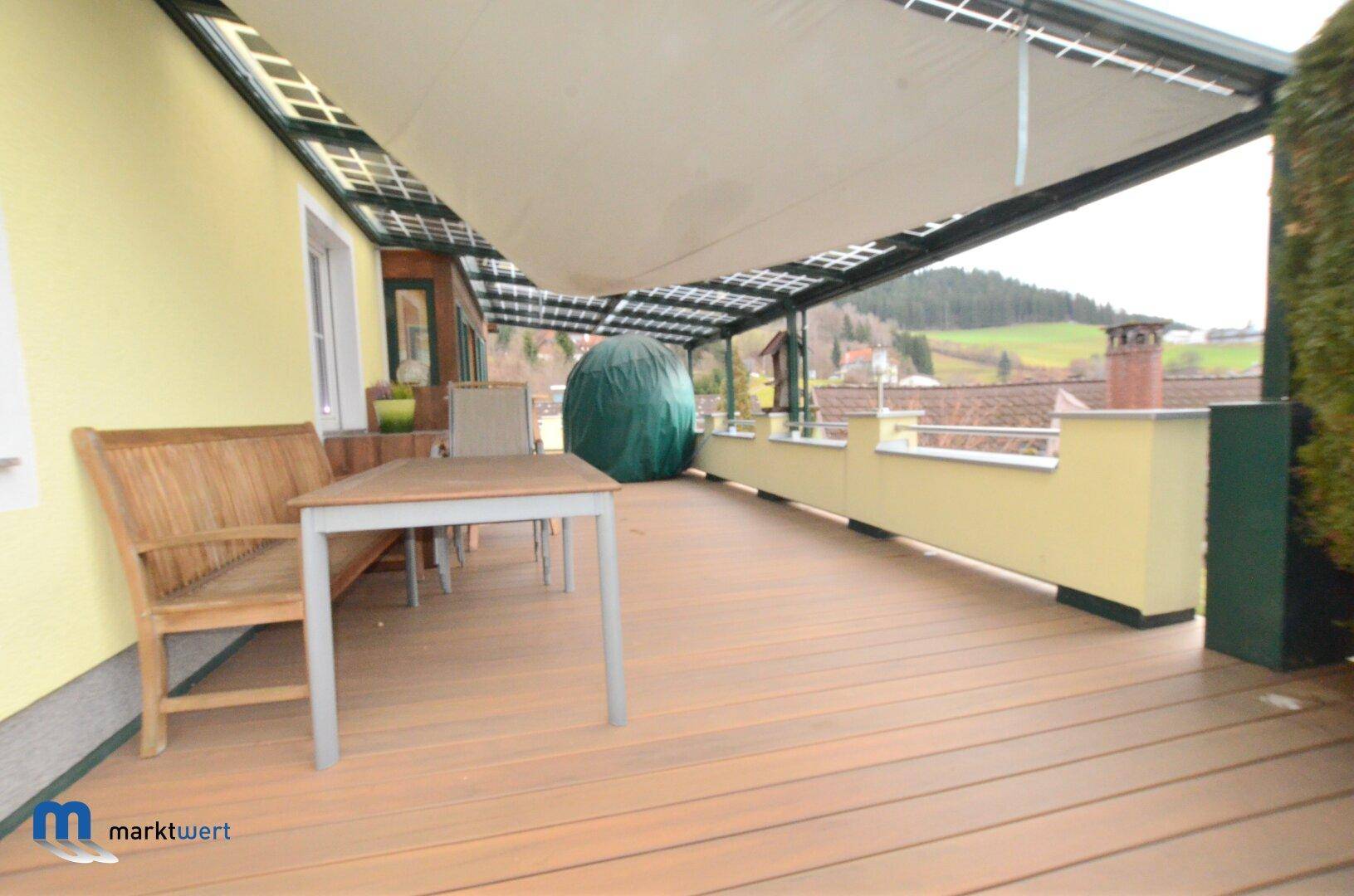 Überdachte Terrasse mit Holzdielenboden, Gartenmöbeln und weitem Blick ins Grüne.