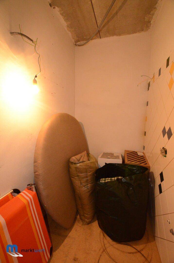 Dunkler Abstellraum mit verschiedenen Gegenständen und sichtbaren Fliesen an der Wand.