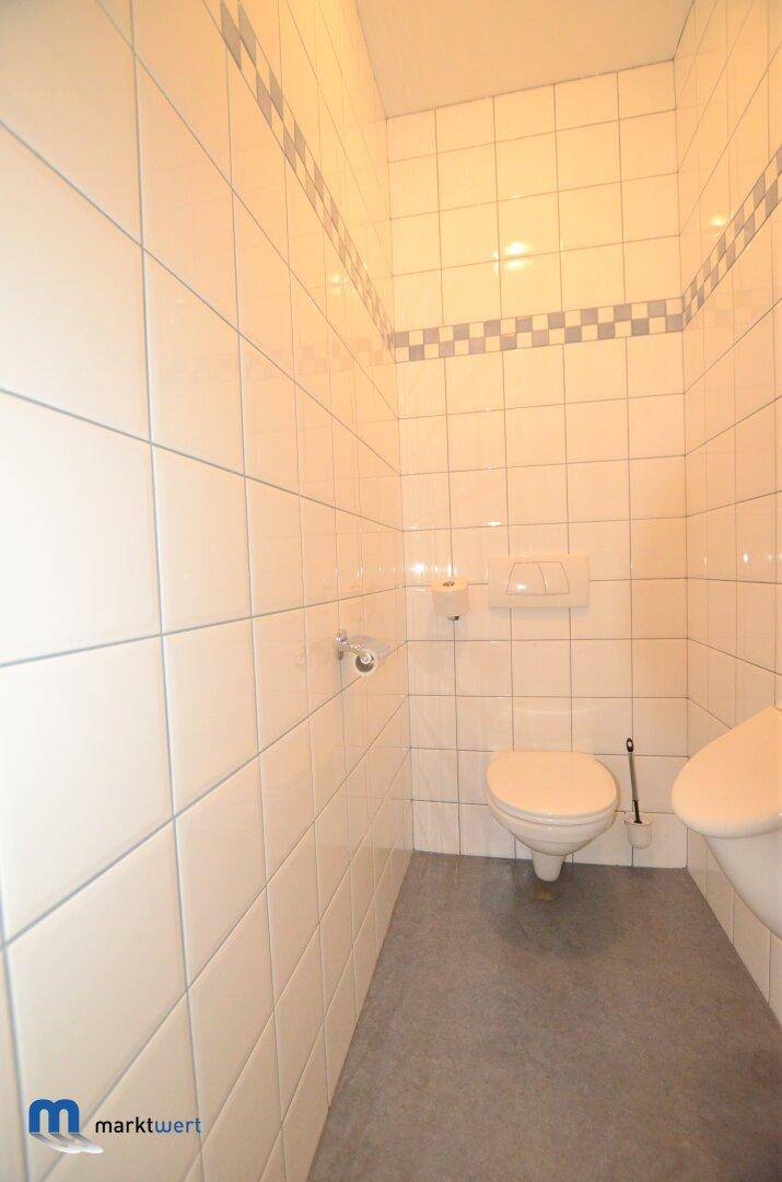 Kleines WC mit gefliesten Wänden, Toilette und einem Teil des Waschbeckens.