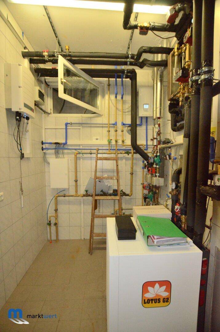 Technikraum mit zahlreichen Rohrleitungen, Steuerungselementen und einem Fenster.