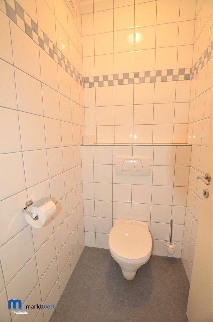 Heller Toilettenraum mit weißen Fliesen, einem Wand-WC und schlichtem Design.
