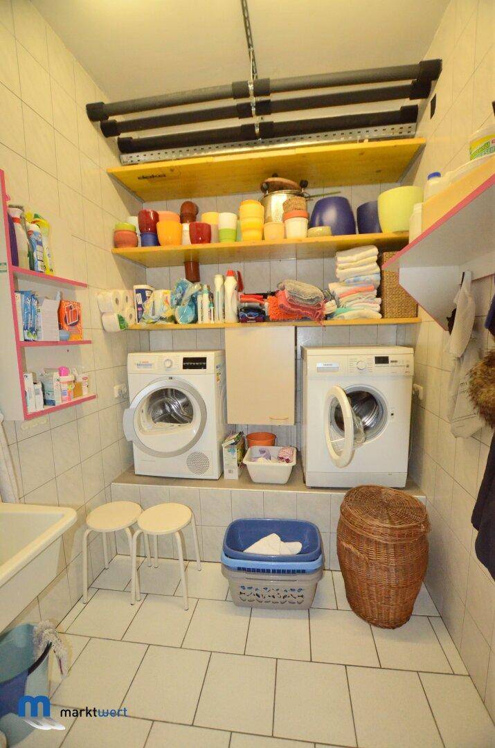 Praktischer Waschraum mit Waschmaschinen, Trockner, Regalen und einem Waschbecken.