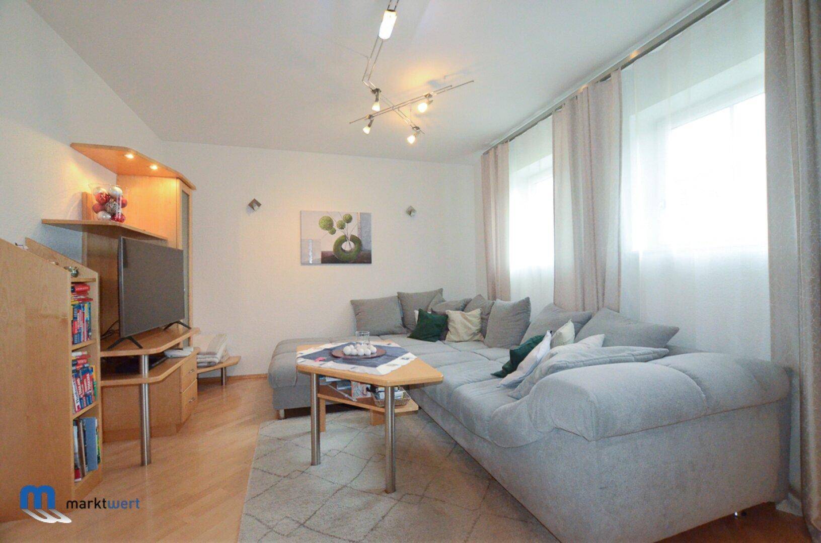 Helles Wohnzimmer mit großem Ecksofa, Couchtisch und Fenstern mit Vorhängen.