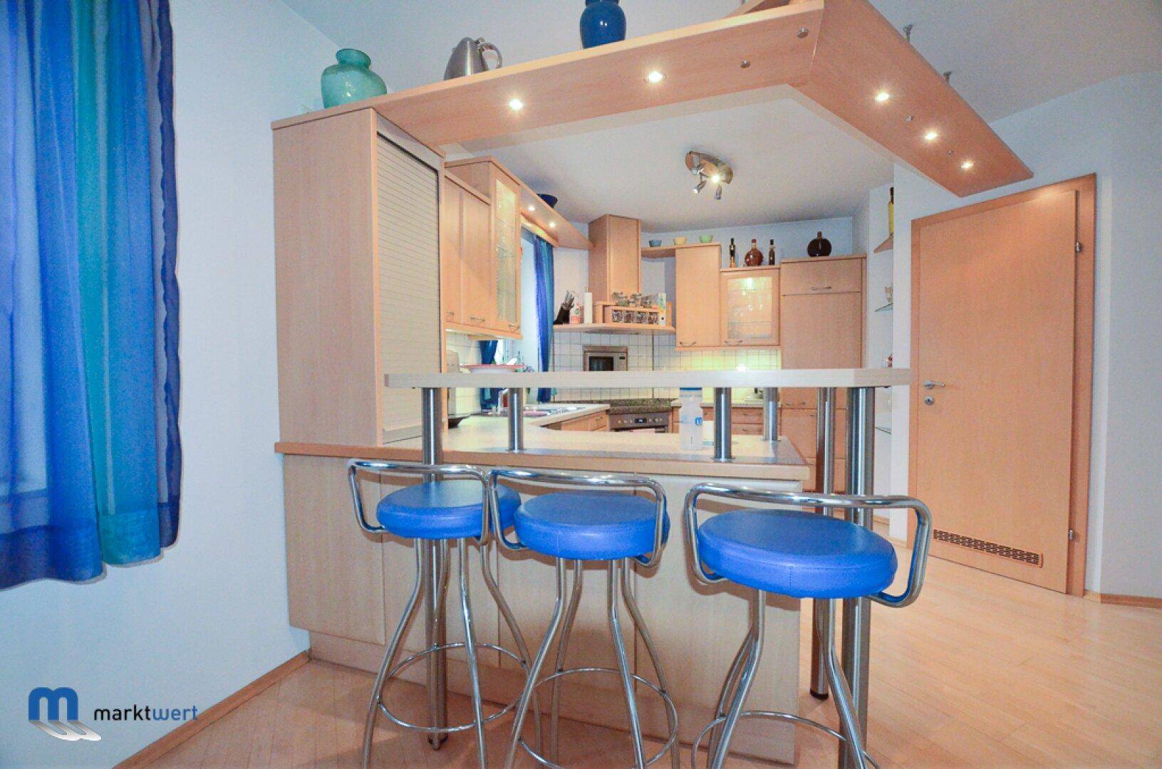Moderne Küche mit heller Holzeinrichtung, Frühstücksbar und blauen Barhockern.