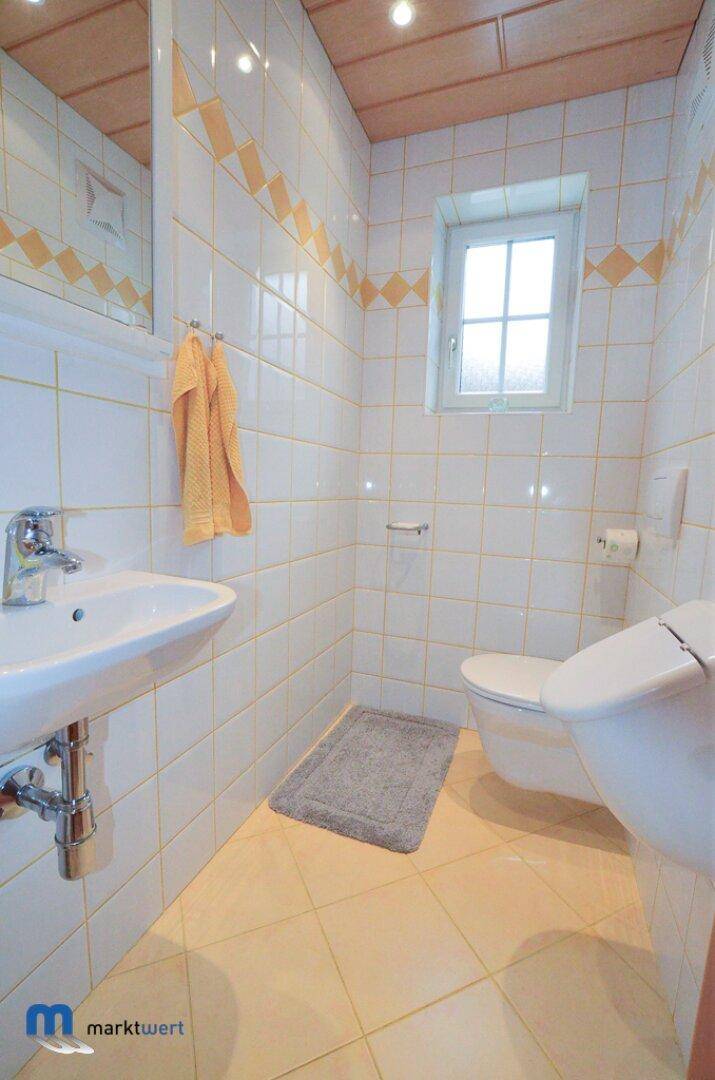 Kleines Badezimmer mit gelb-weißen Fliesen, Waschbecken und Toilette.