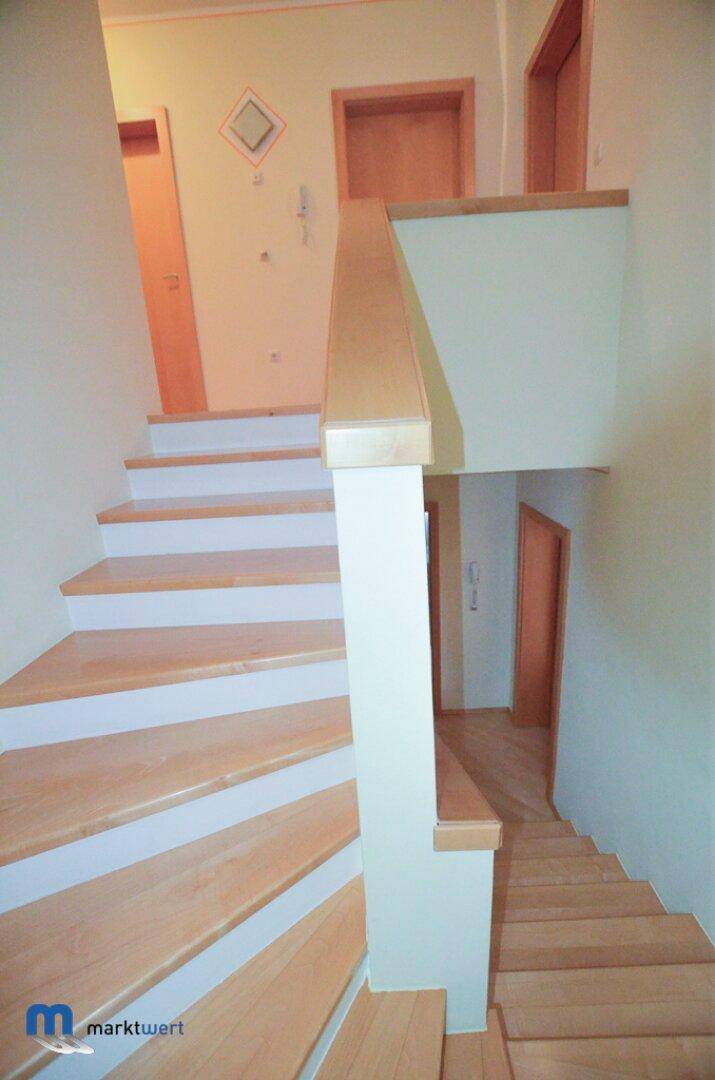 Helle Holztreppe mit weiß gestrichenen Setzstufen, die die Stockwerke verbindet.