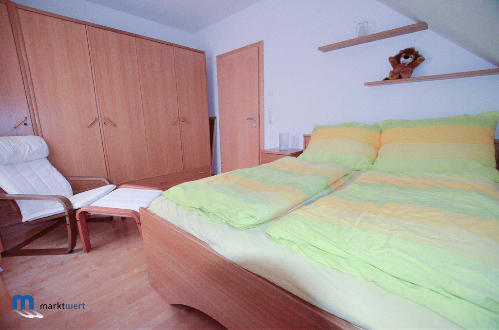 Schlafzimmer mit Holzbett, großem Kleiderschrank und bequemen Sessel unter Dachschrägen.