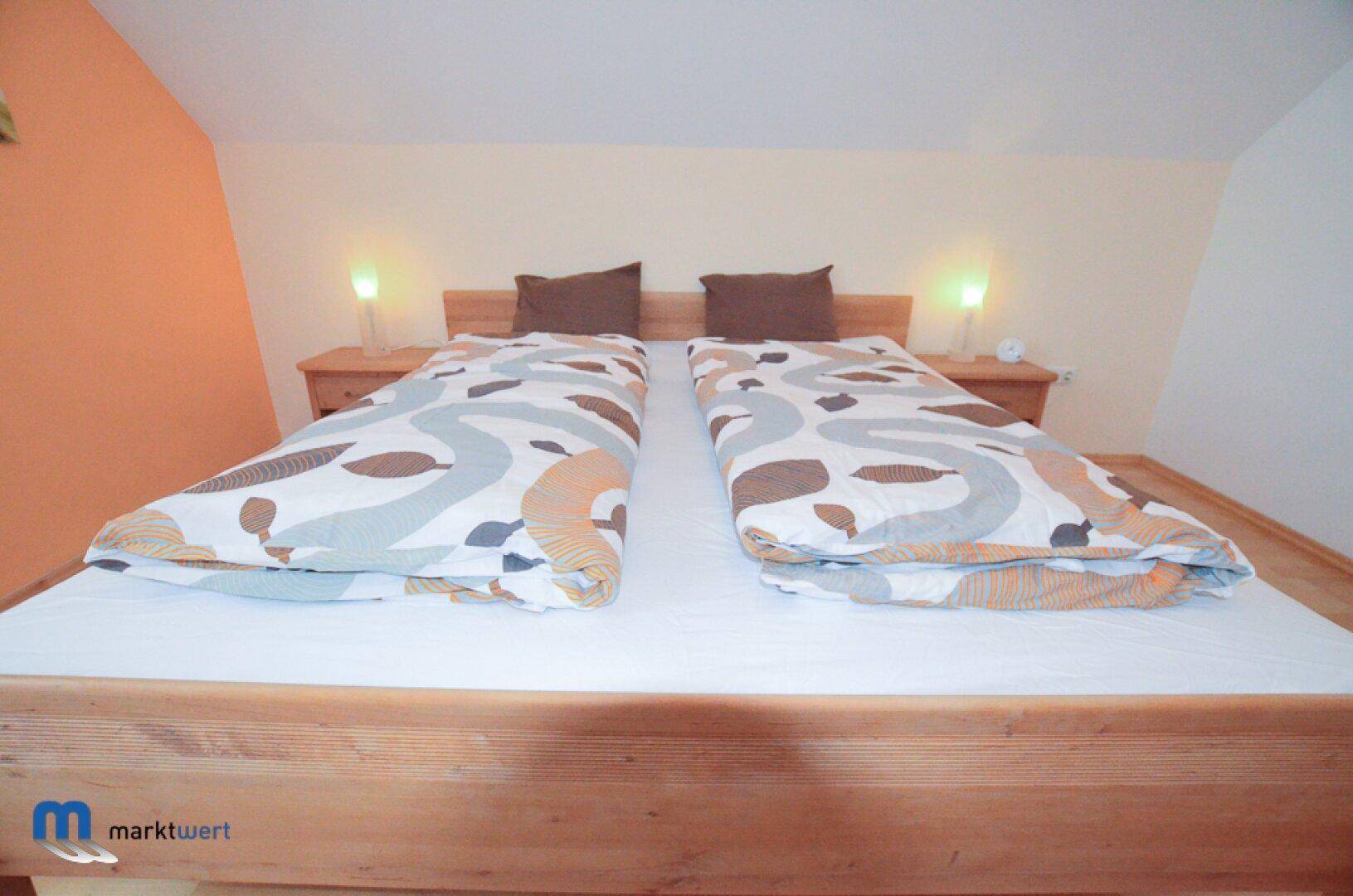 Schlafzimmer mit Holzbett, Nachttischen und farbiger Bettwäsche unter Dachschrägen.