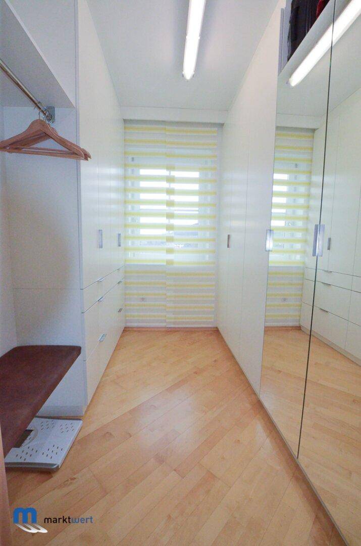 Geräumiger begehbarer Kleiderschrank mit Spiegelfronten und Fenster für Tageslicht.