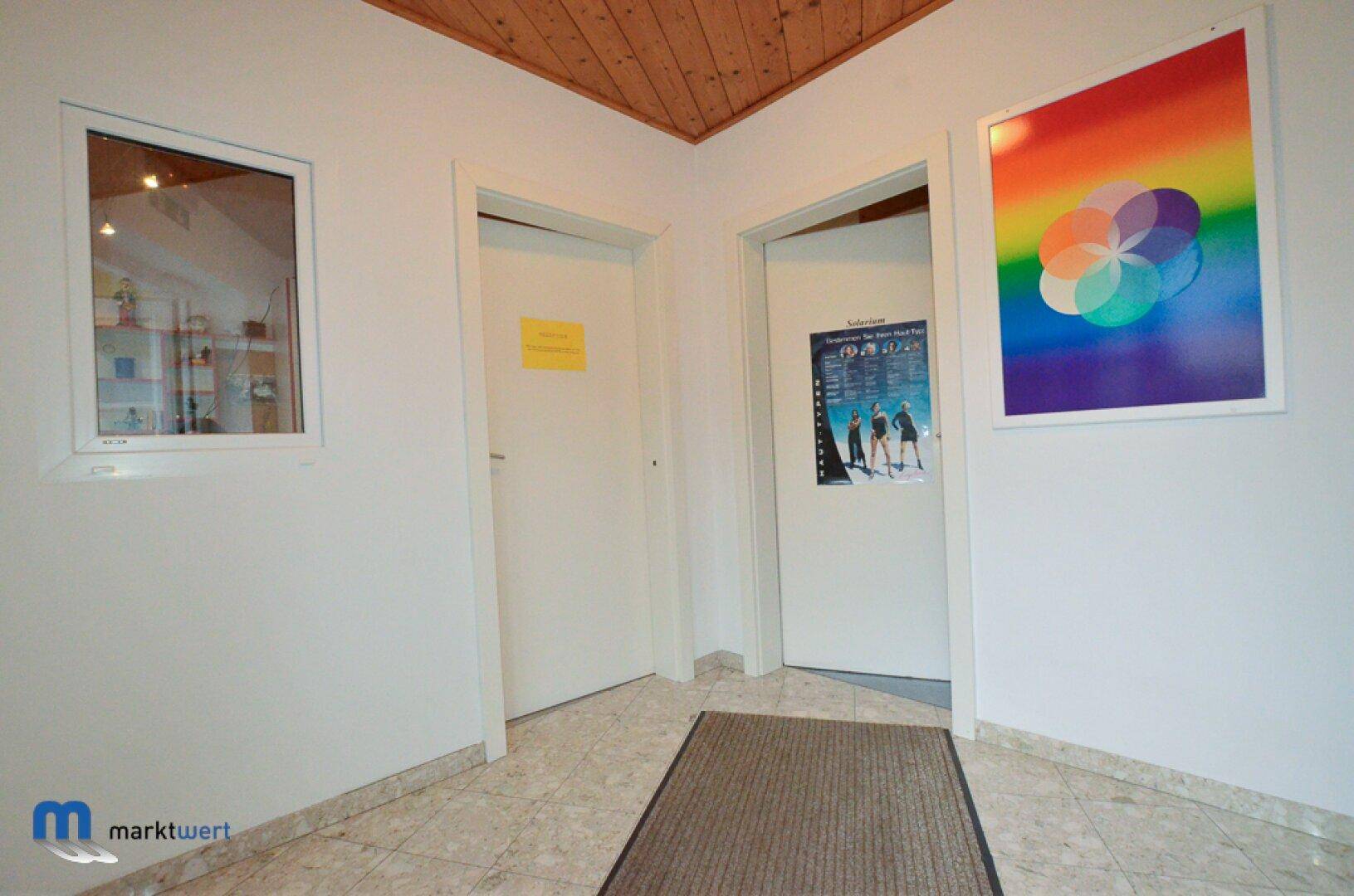 Flur mit mehreren Türen, Fliesenboden, Holzdecke und farbenfrohem Wandbild.