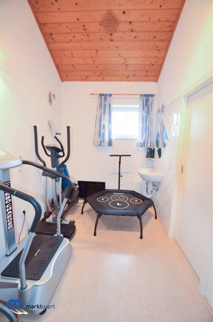 Raum mit Fitnessgeräten, Waschbecken, Fenster und Holzdeckenverkleidung.