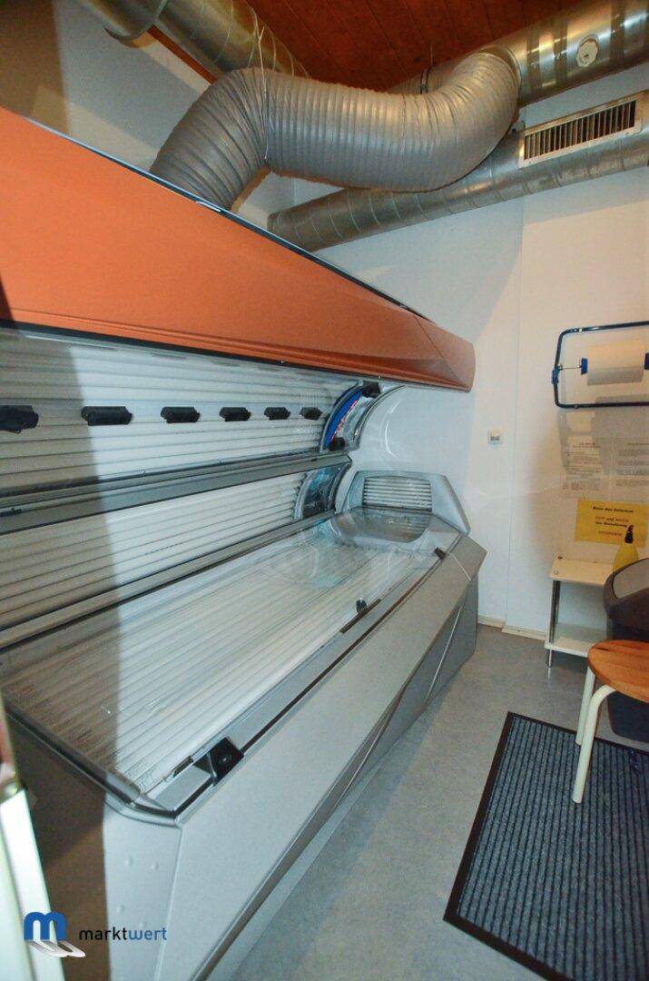 Solariumraum mit orangefarbener Liegefläche, Holzdecke und industriellen Lüftungsrohren.