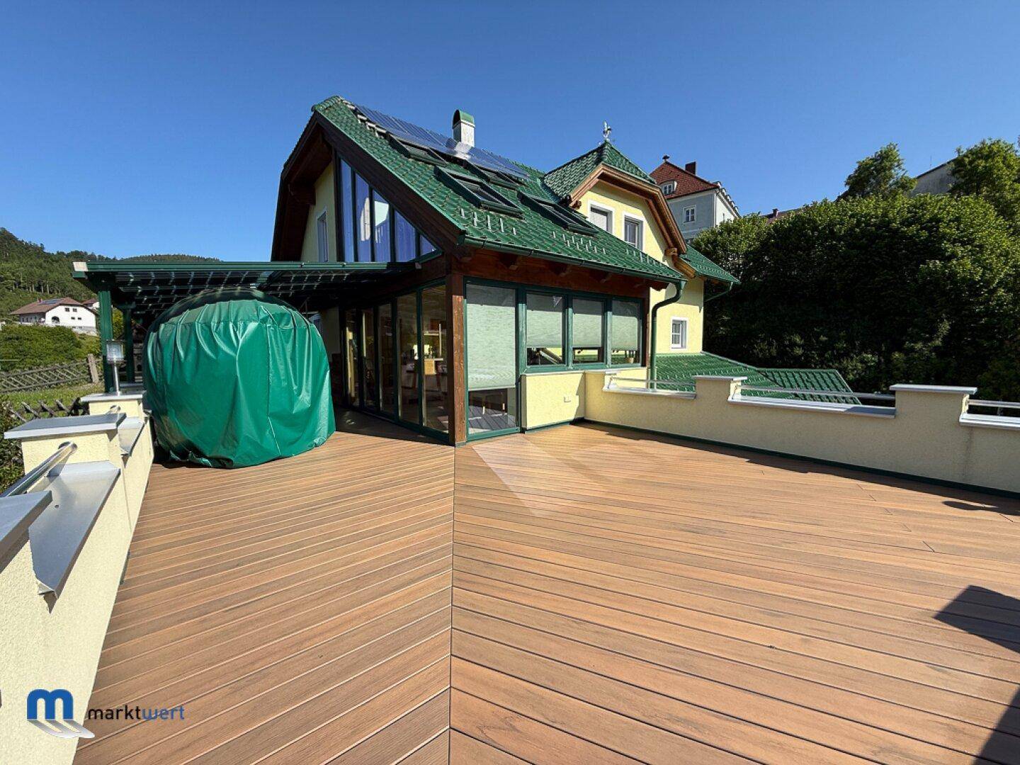 Große Holzterrasse mit Glasanbau und Blick auf die grüne Hügellandschaft.