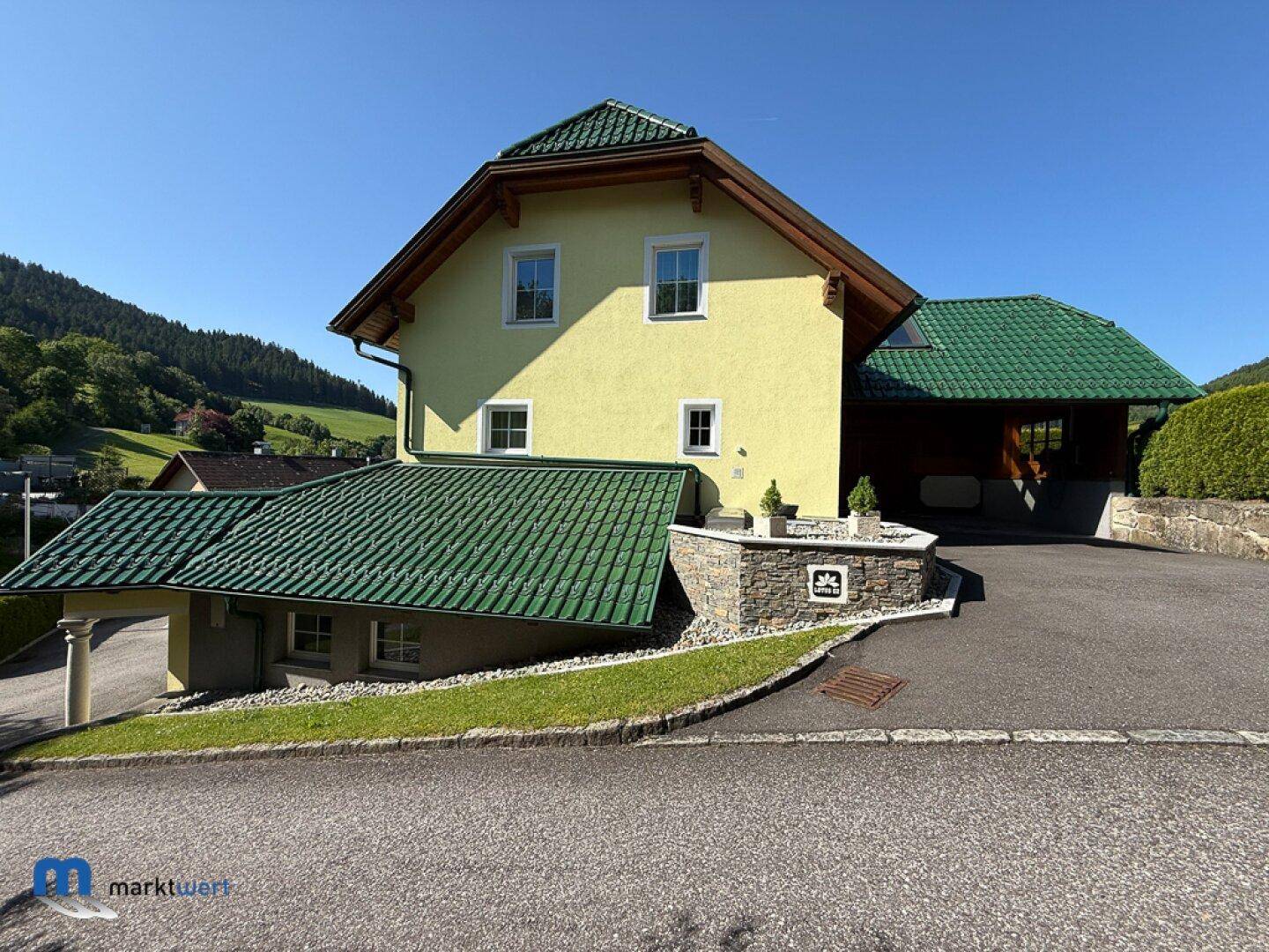 Ansicht des Hauses mit gelber Fassade, grünem Dach und gepflegter Auffahrt.