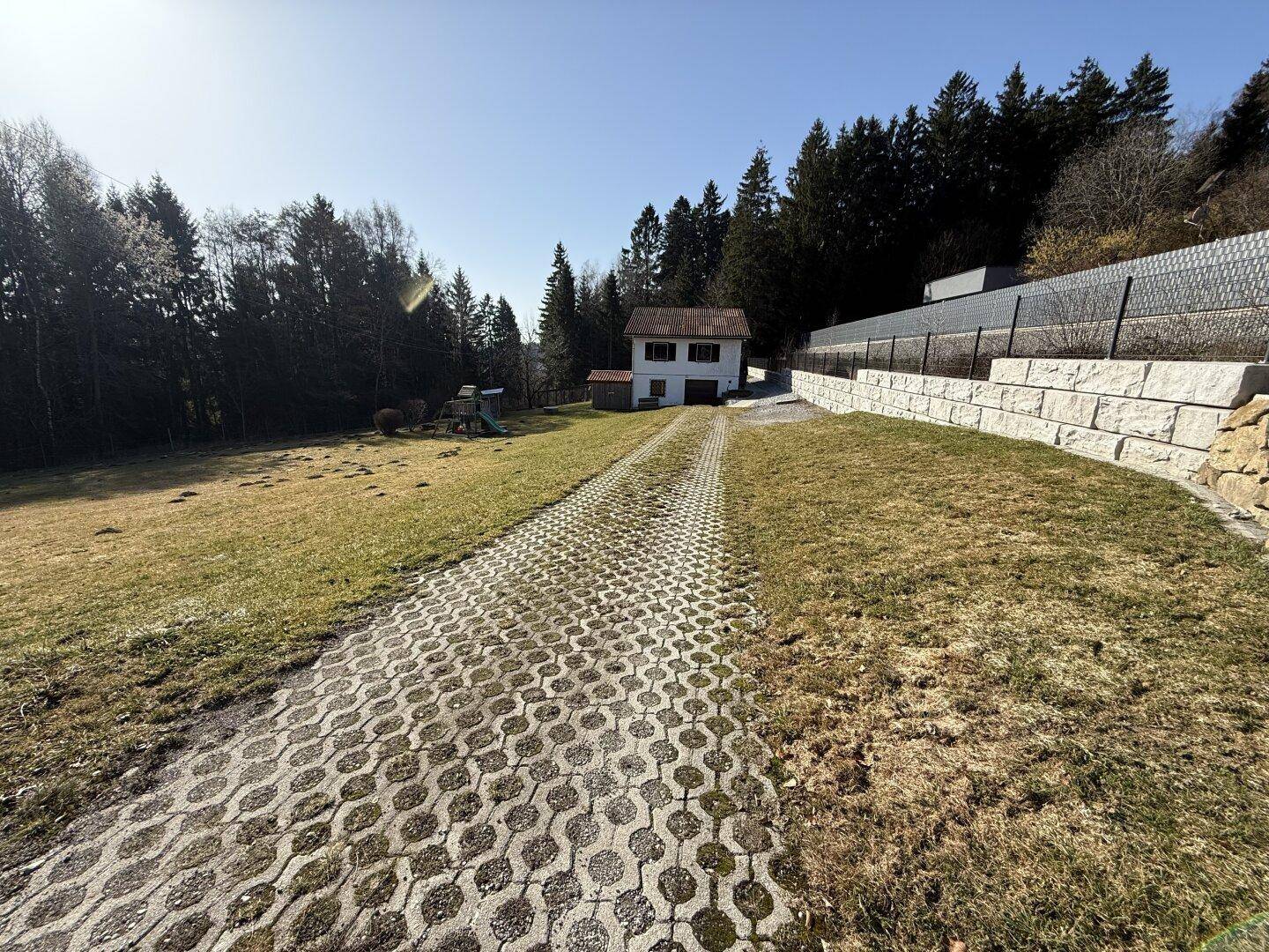 Zufahrt zum Haus mit Rasengittersteinen, umgeben von Wiesen und Wald.