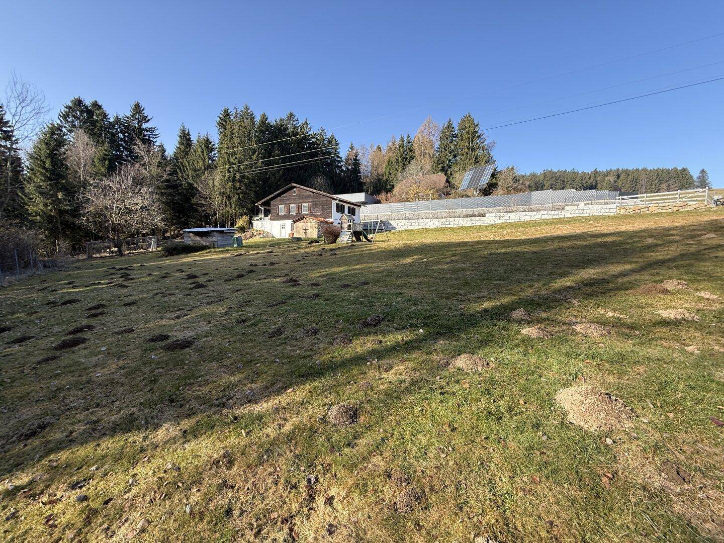Haus in ländlicher Umgebung mit weiten Wiesenflächen und dichtem Wald im Hintergrund.