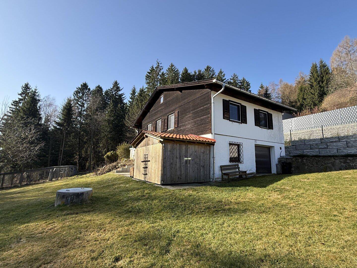 Seitenansicht des Hauses mit weißer Fassade, Holzverkleidung und einem kleinen Schuppen.
