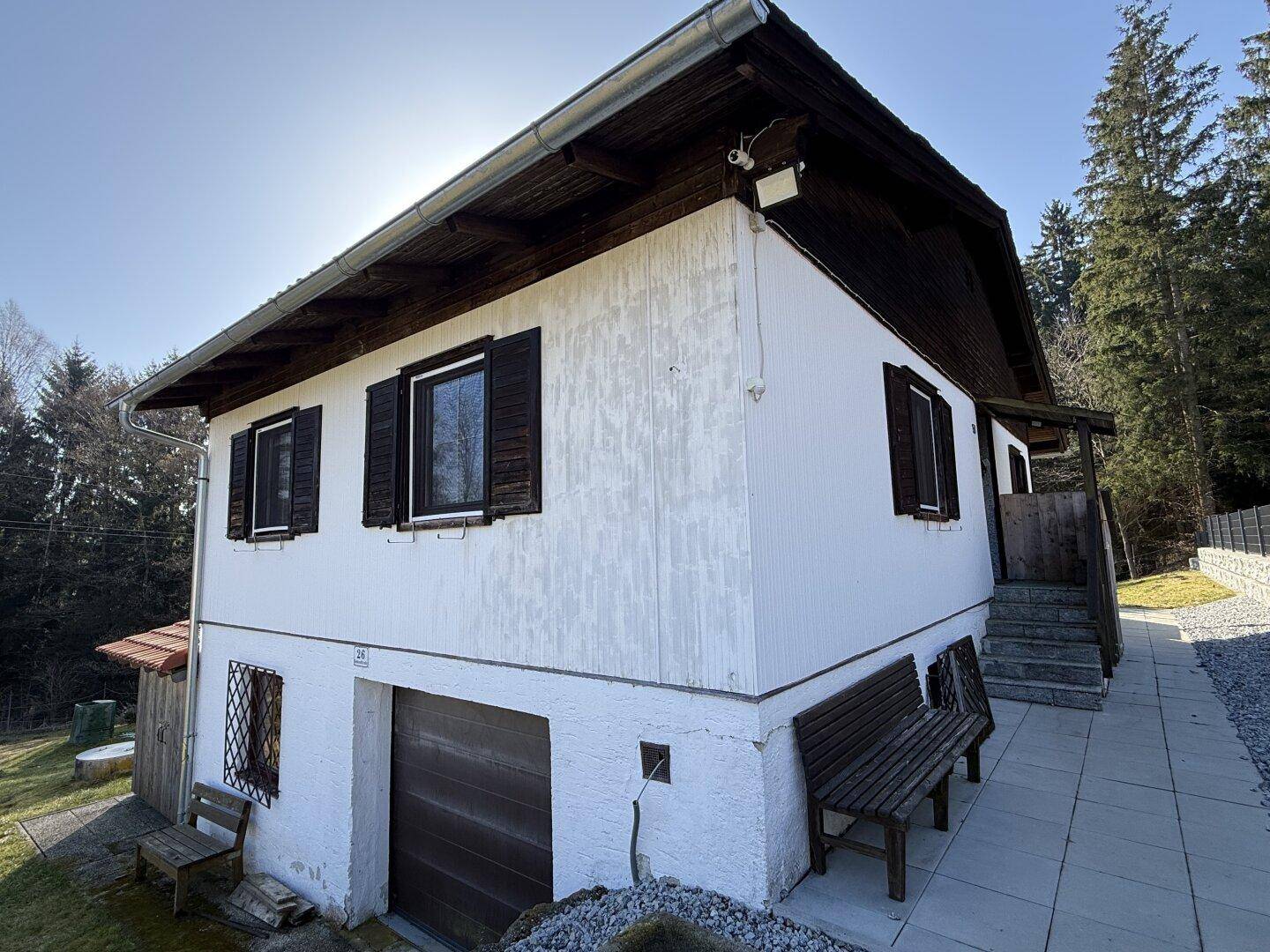 Vorderansicht des Hauses mit weißer Fassade, Holzfensterläden und integrierter Garage.