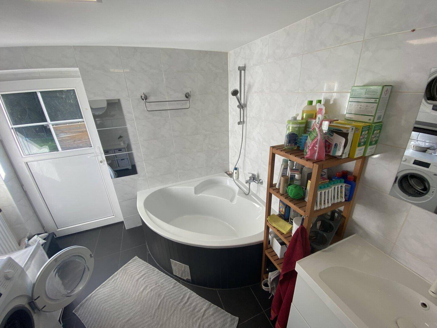 Badezimmer mit Eckbadewanne, Duscharmatur und praktischem Regal für Badutensilien.