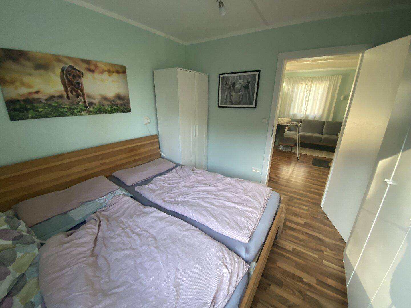Schlafzimmer mit Holzbett, Kleiderschrank und Blick in den angrenzenden Wohnbereich.