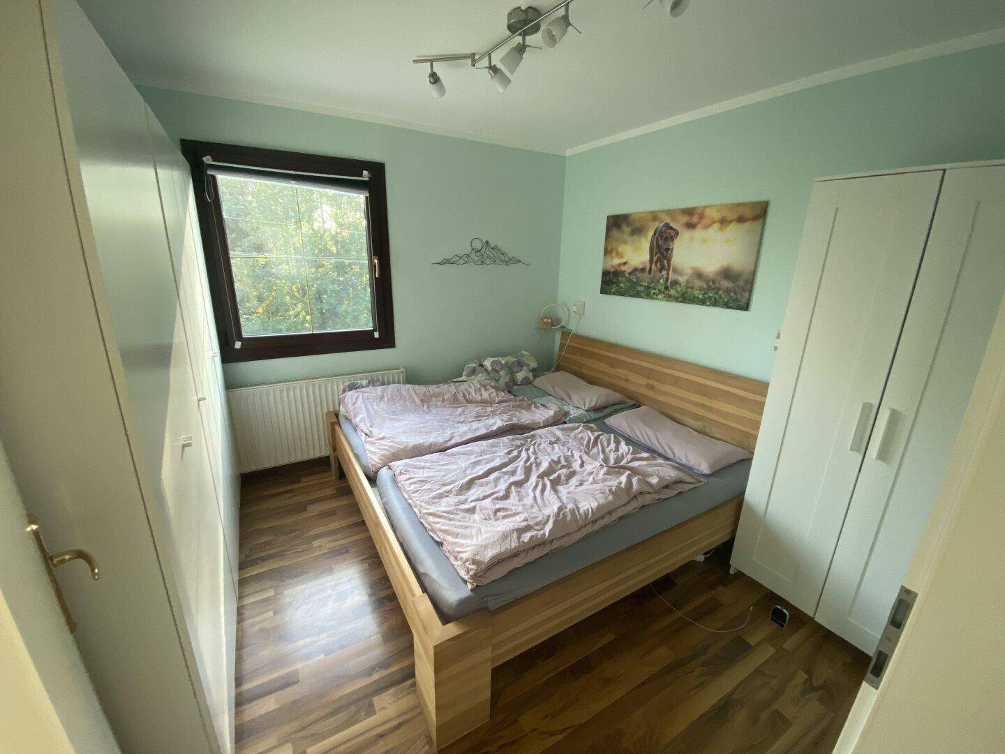 Helles Schlafzimmer mit Holzbett, Kleiderschränken und Fenster mit Blick ins Grüne.