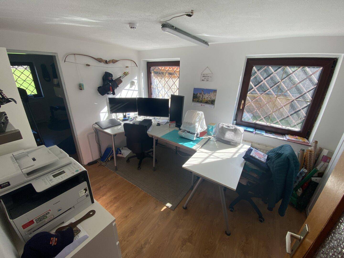 Helles Heimbüro mit mehreren Monitoren, Schreibtischen und Fenstern für Tageslicht.